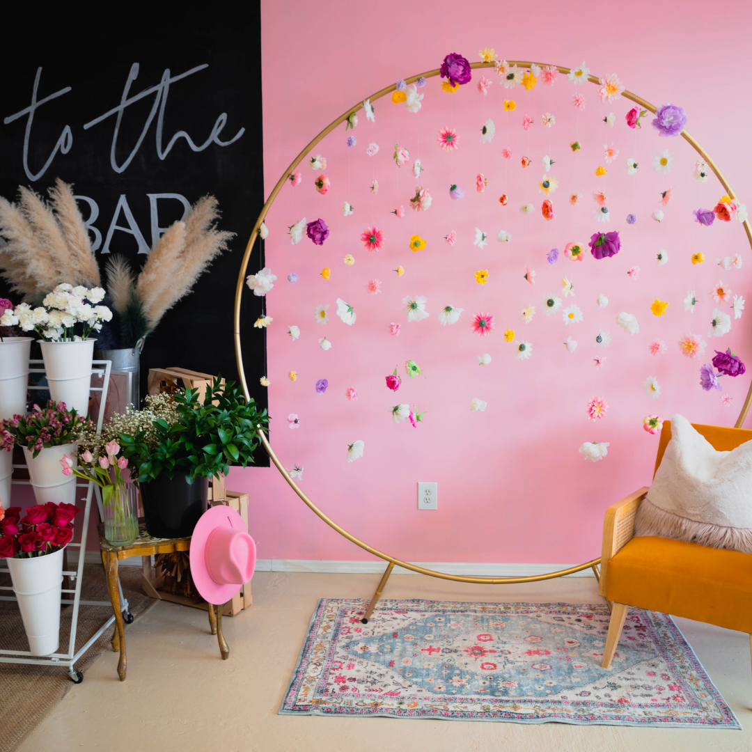 Fleur de Mer flower bar with pink wall, hanging floral installation on gold hoop, and mustard chair